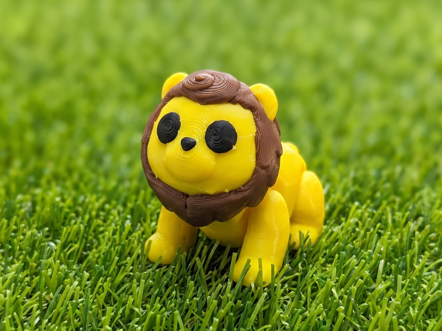 A single Mini Printie — the yellow lion flexi figure sitting on grass
