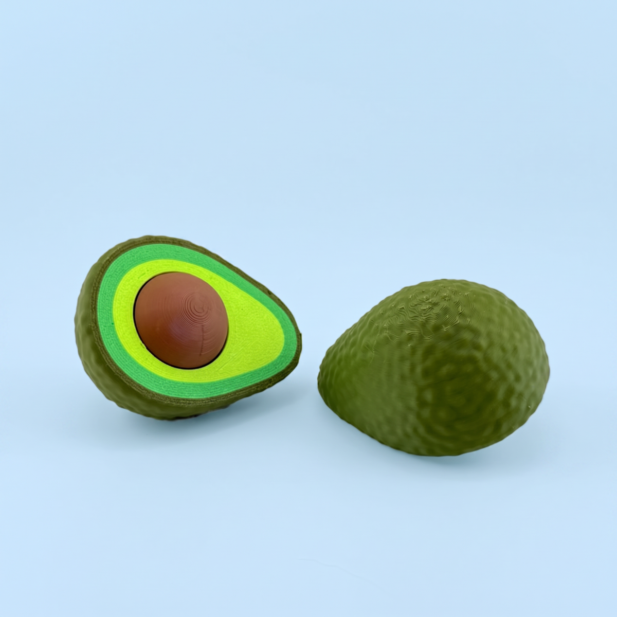 Avocado fidget clicker beside the closed whole avocado half