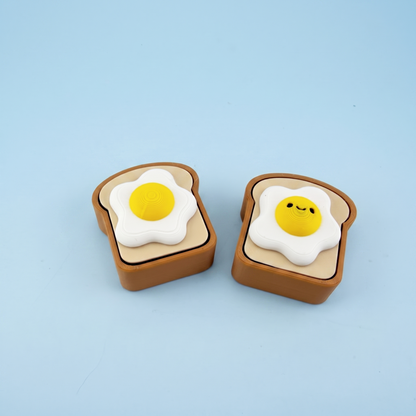 Egg on toast fidget clickers, one plain and one with a smiley yolk