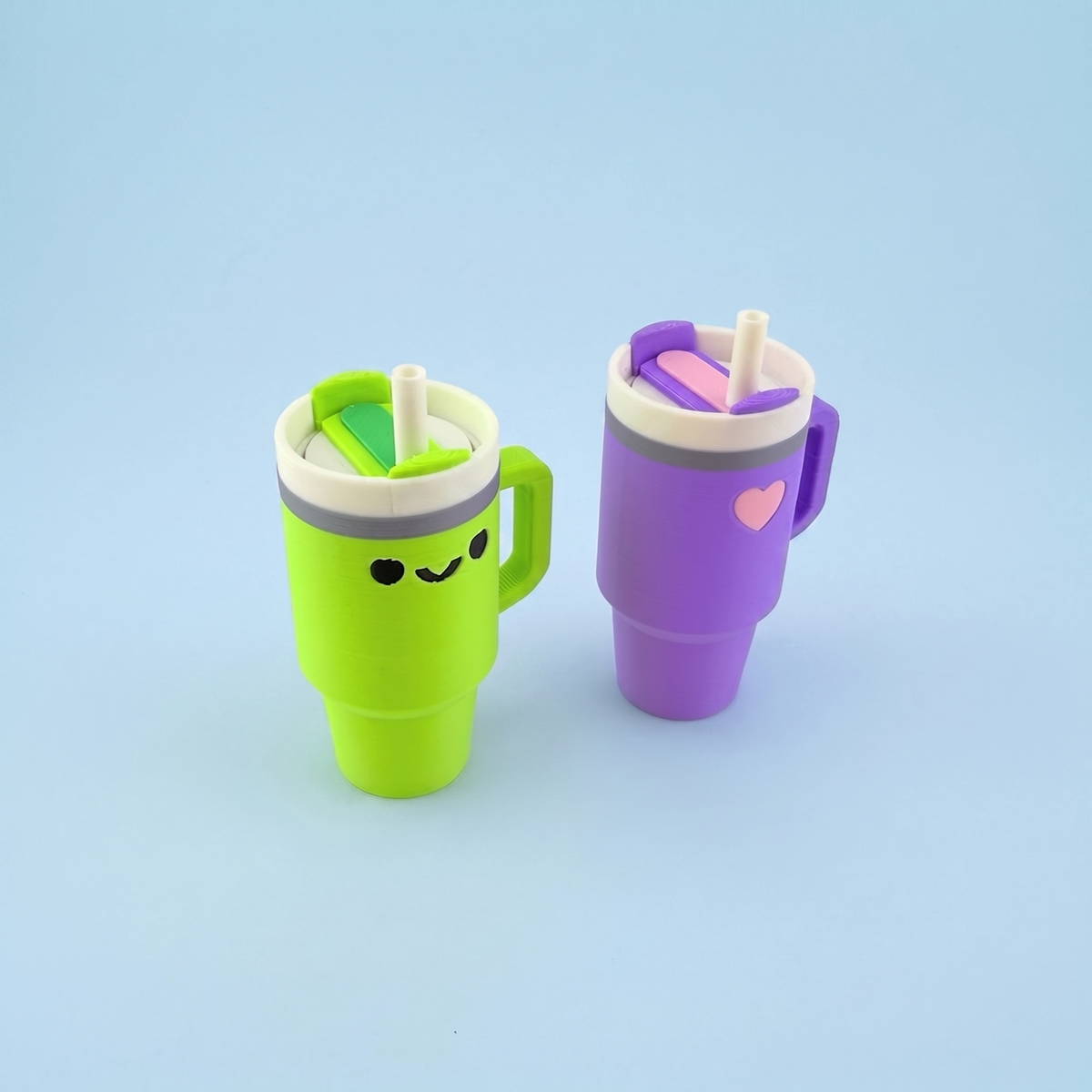 Matcha tumbler with a smiley face beside a lilac tumbler with a heart