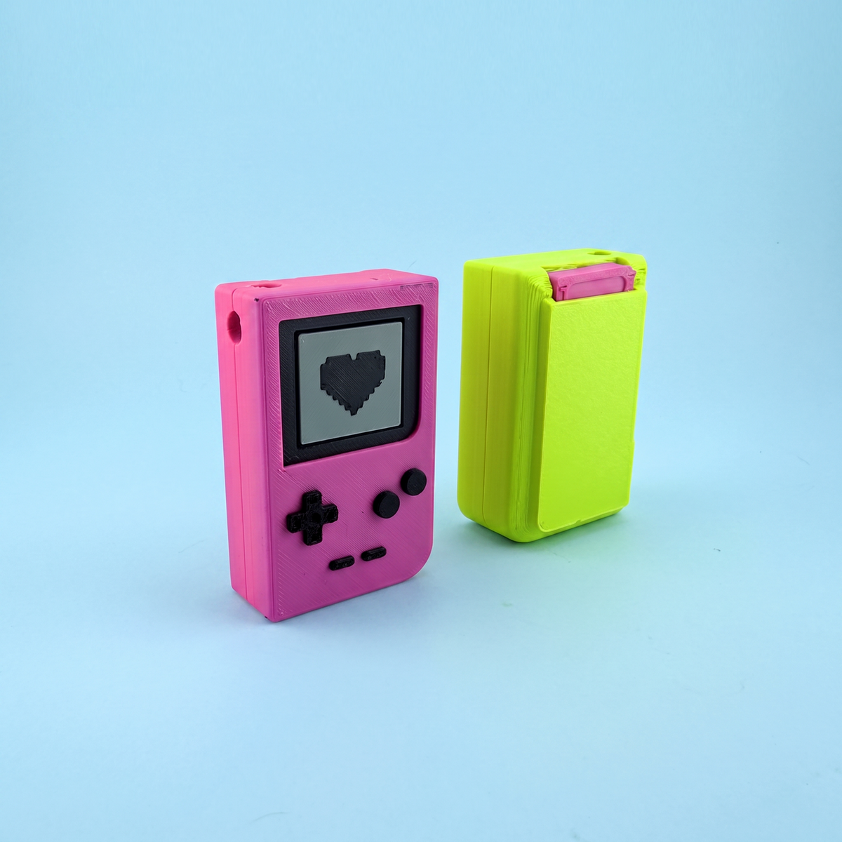 Pink pocket console with a pixel heart screen beside a neon yellow one